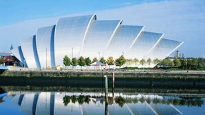 Un bâtiment moderne au design original, caractérisé par ses lignes courbes, qui se reflète dans les eaux calmes d’un plan d’eau.