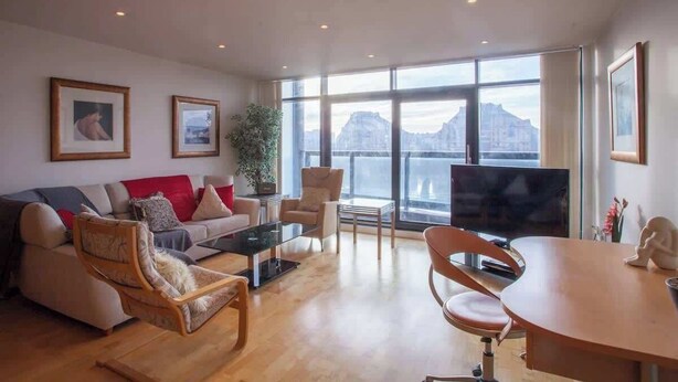 Un salon spacieux comprenant un canapé, des fauteuils, une table basse et un téléviseur. De grandes fenêtres offrent une vue sur les montagnes.