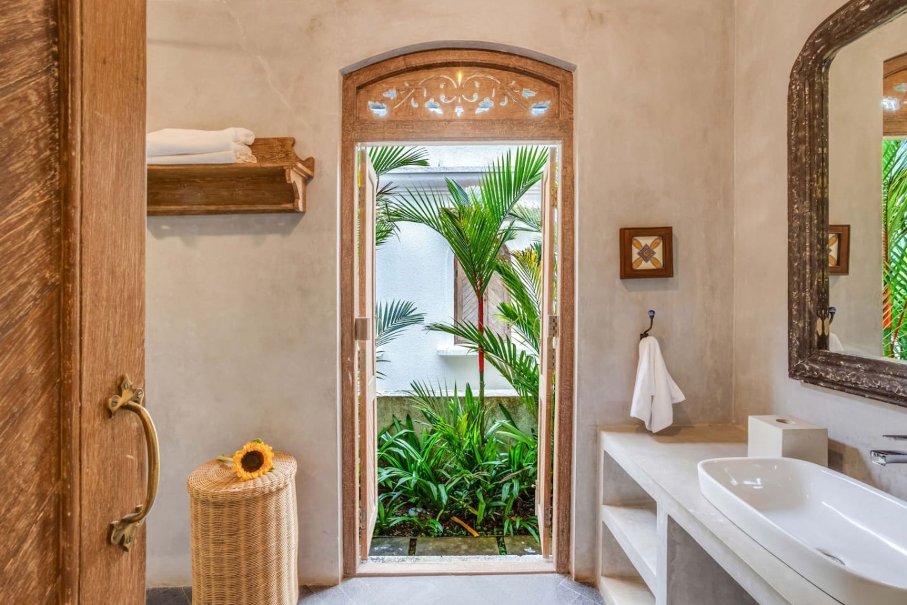 A bathroom with a wooden door, a white sink, a mirror, and a small plant.
