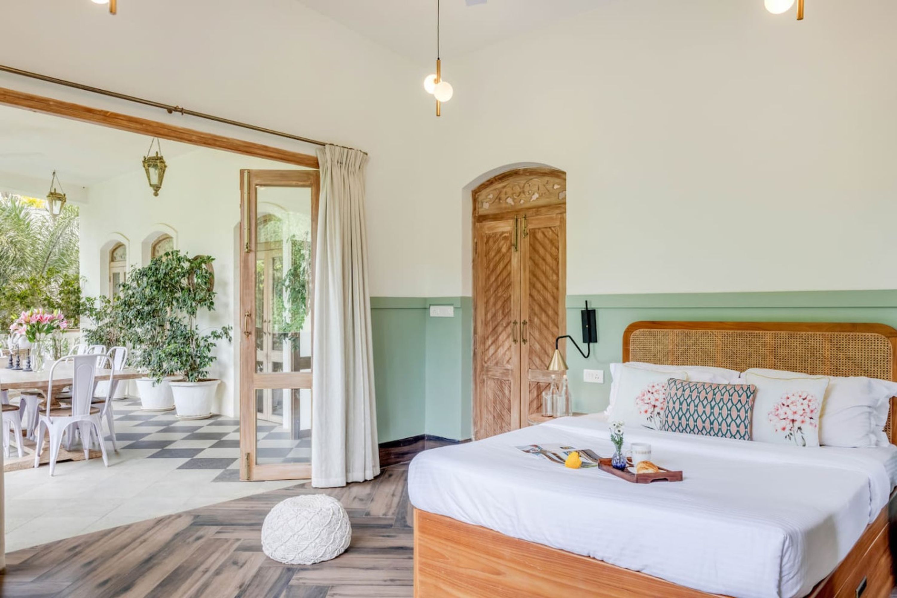 A bedroom with a wooden bed, a dining area with white chairs, a large window with curtains, and a green wall.