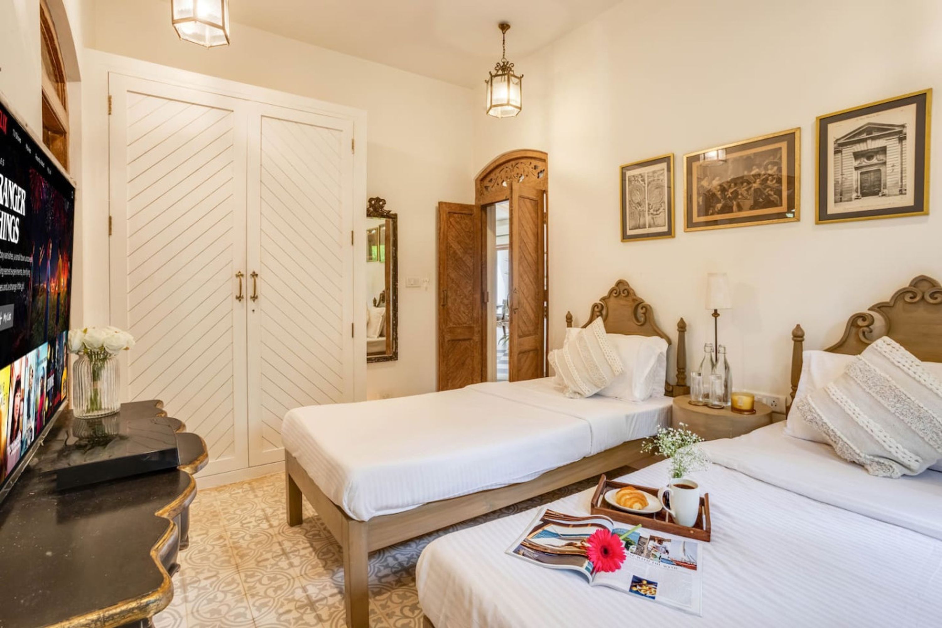 Une chambre d’hôtel avec un grand lit, un plus petit lit, un bureau avec un ordinateur, une armoire et des tableaux encadrés au mur.