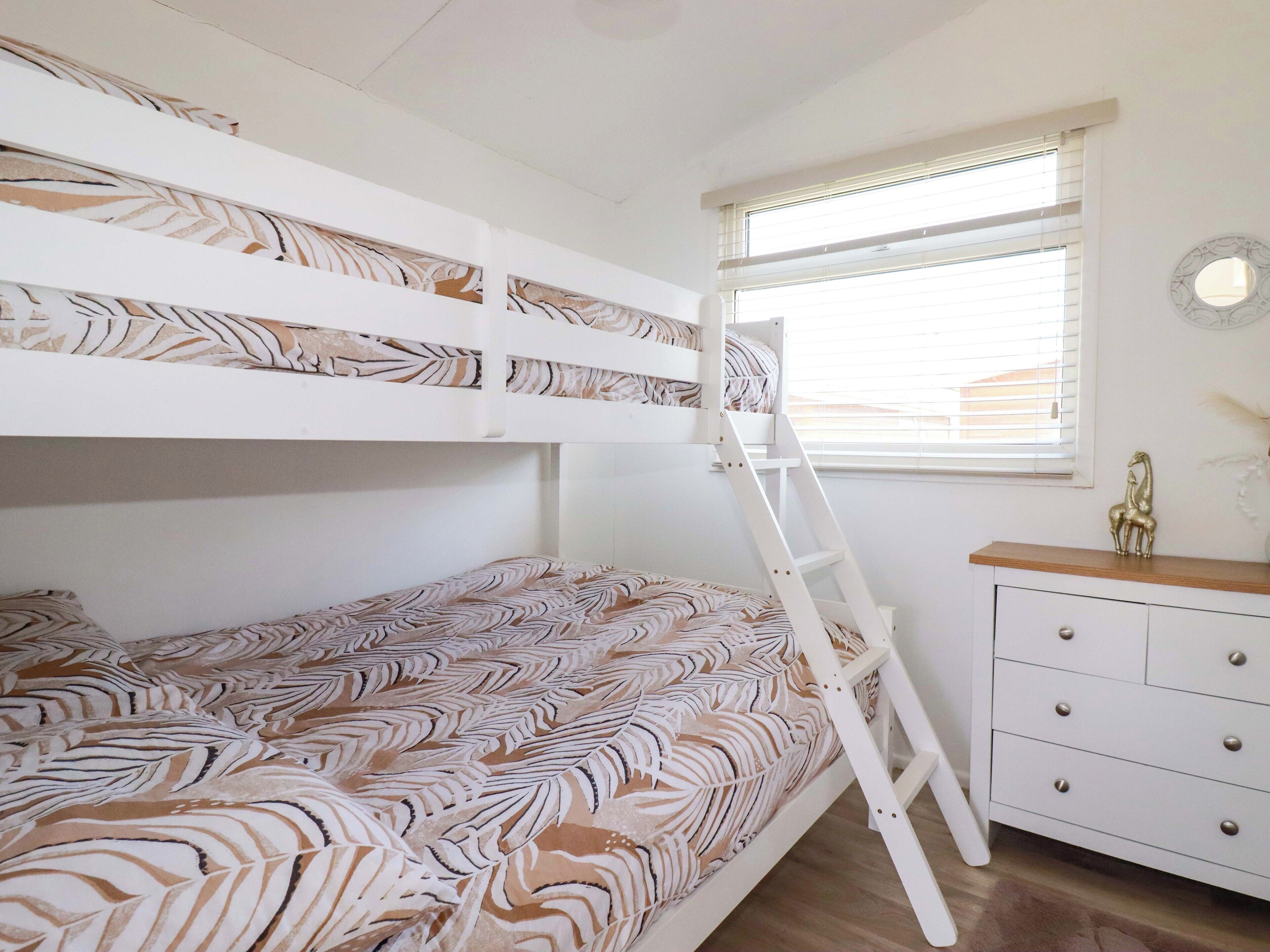 A bunk bed room with a ladder, a window with blinds, and a dresser with drawers.