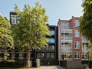 En modern hyresfastighet med ett träd framför, en grind vid entrén och en cykel parkerad utanför.
