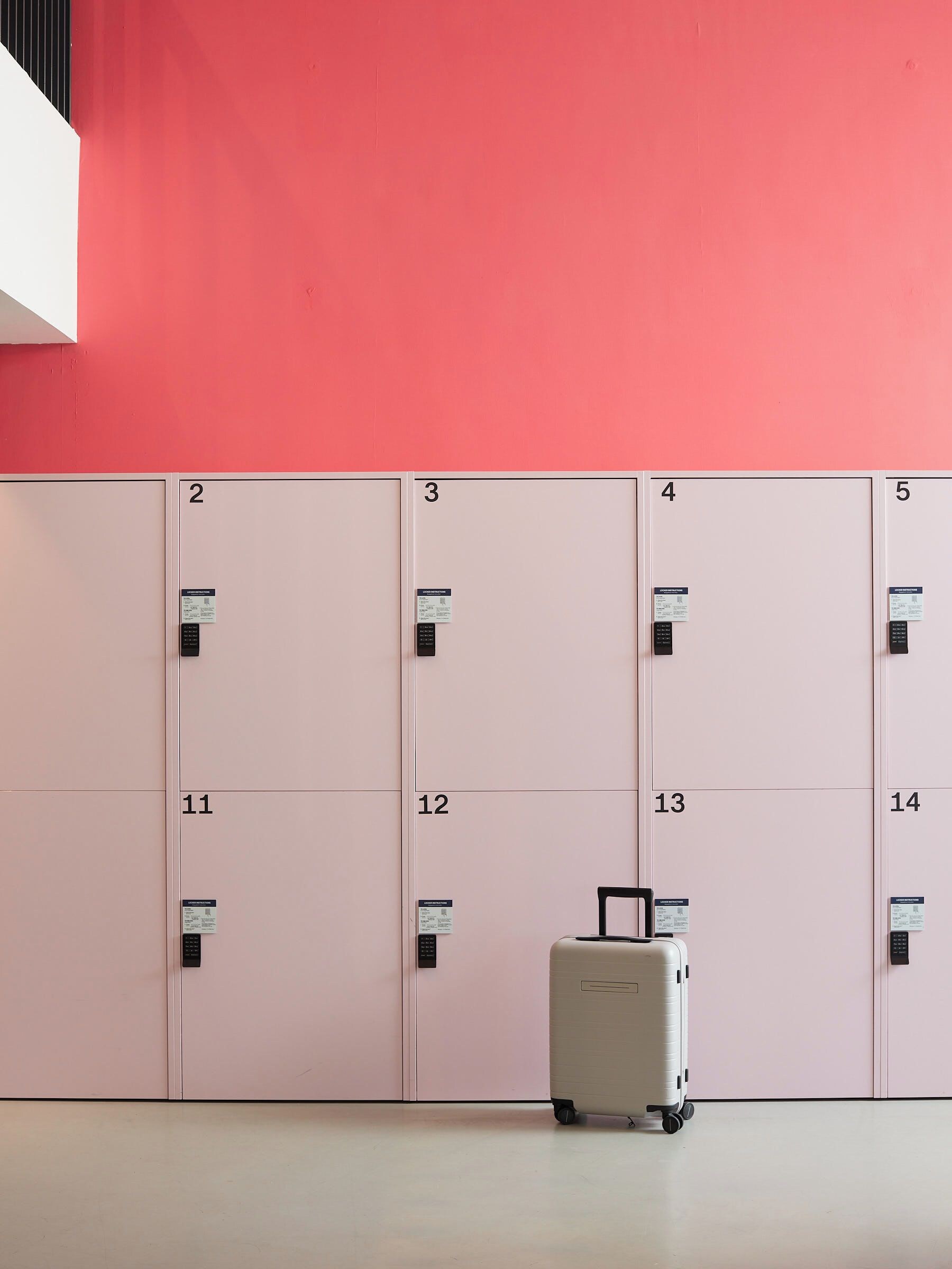 Een rij lockers genummerd van 2 tot 14 tegen een roze muur, met een koffer voor locker nummer 13.