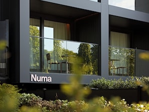En modern byggnad med stora fönster, ett väl synligt utomhusområde med sittplatser och namnet ”Numa” på fasaden.