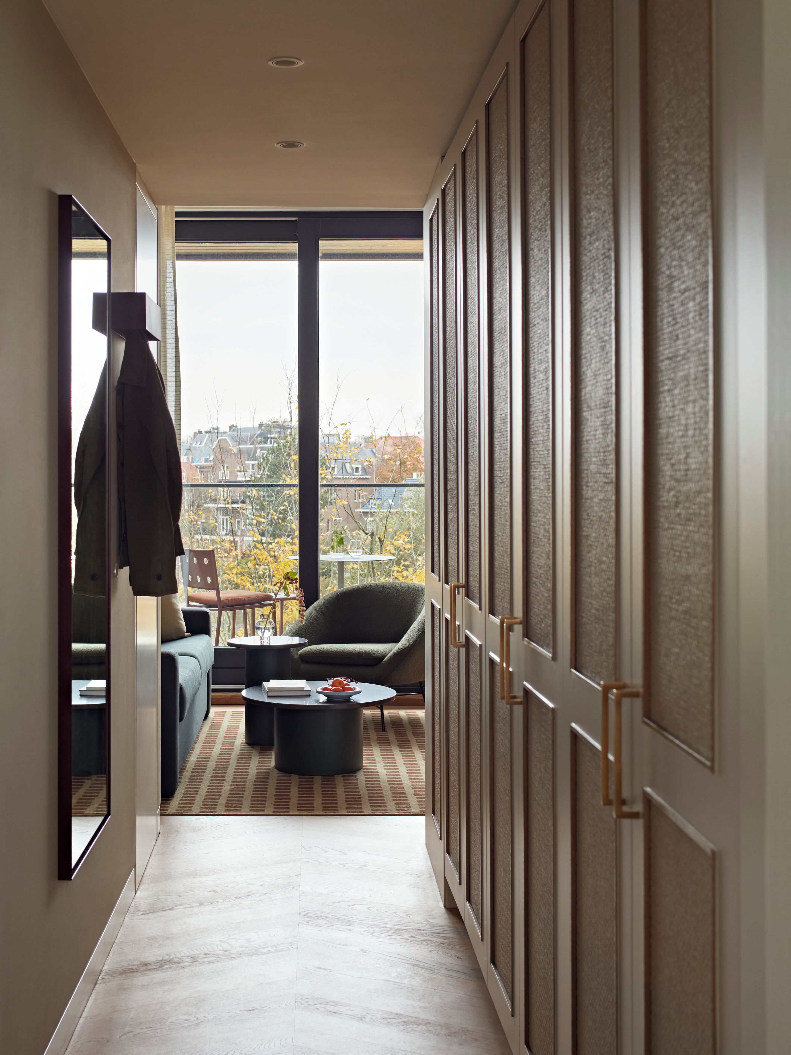 A hallway with a view of the city, a sofa, a chair, and a coffee table.
