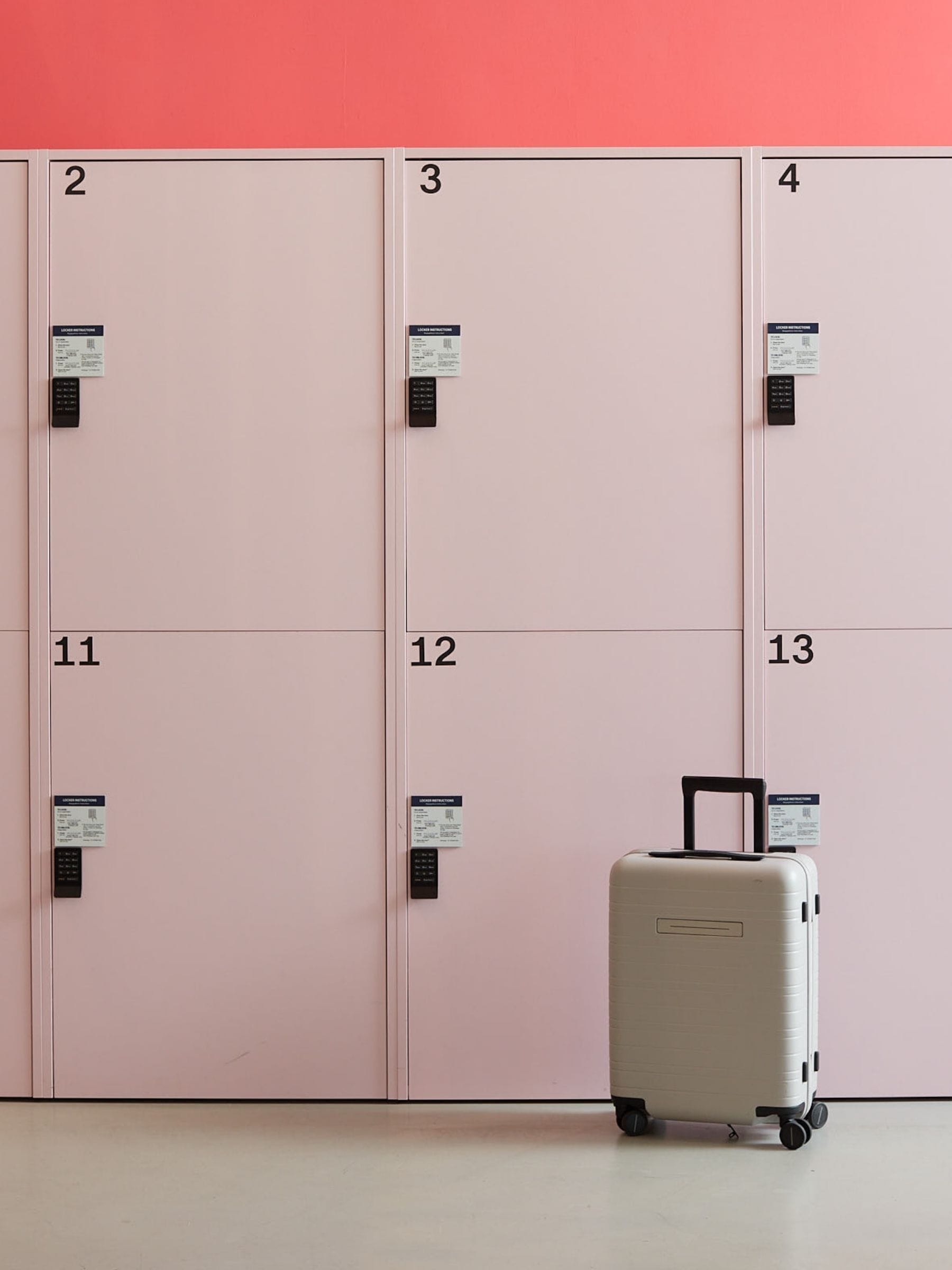 A row of pink lockers numbered 2 to 13, with a suitcase placed in front of locker number 13.