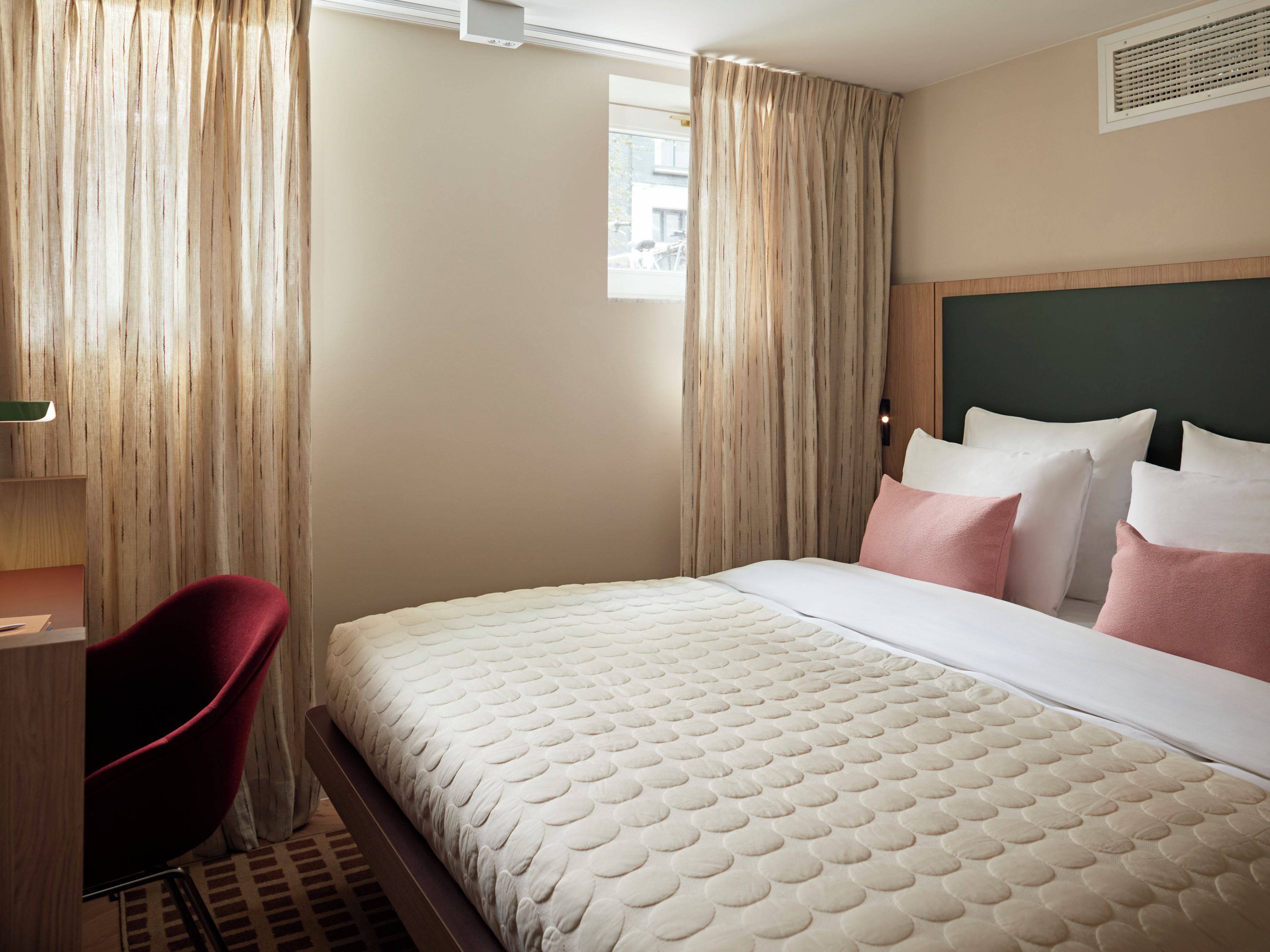 Una habitación de hotel con cama, escritorio, silla y ventana con cortinas.