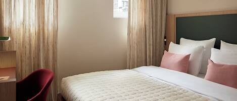 Una habitación de hotel con cama, escritorio, silla y ventana con cortinas.