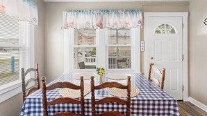 A dining area with a checkered tablecloth, wooden chairs, a ceiling fan, and a window with blinds. - Shannon A - downstairs (Ocean City)