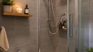 Une salle de bain moderne dotée d’une douche à parois de verre, d’un bidet et d’une étagère où sont rangés les articles de toilette.