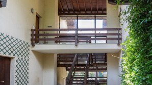 Un espacio al aire libre cubierto con una escalera de madera que conduce a un balcón, rodeado de follaje.