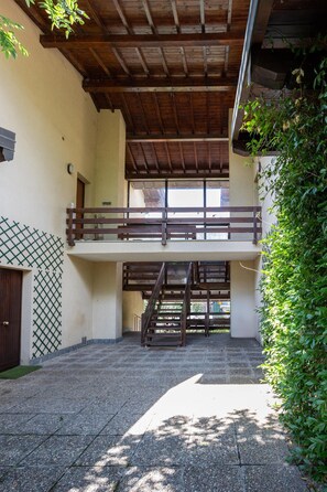A covered outdoor area with a wooden staircase leading to a balcony, surrounded by greenery. - Apartment 'Rocca Lake House' with Shared Garden, Balcony and Wi-Fi (Angera)