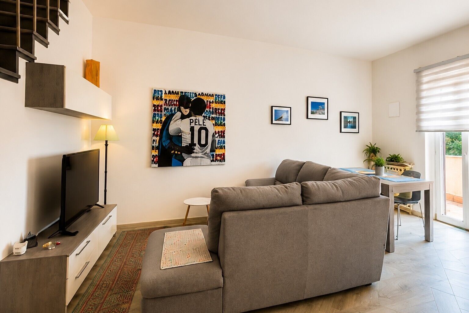Een moderne woonkamer met een bank, een flatscreen televisie, een eethoek met een tafel en stoelen, en een trap.