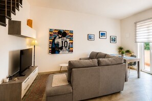 A modern living room with a sofa, a flat-screen TV, a dining area with a table and chairs, and a staircase.