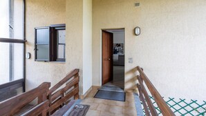 Un pasillo con bancos de madera, una puerta que da a una habitación y una ventana con persianas.