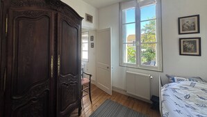 A bedroom with a large wooden wardrobe, a bed with a patterned duvet, a radiator, and a window with a view of greenery outside. - La Rochelle -House with billiard table (La Rochelle)