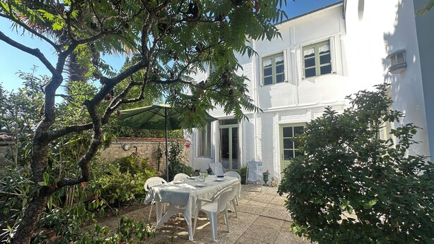 A patio with a table and chairs, surrounded by potted plants and a white building. - La Rochelle -House with billiard table (La Rochelle)