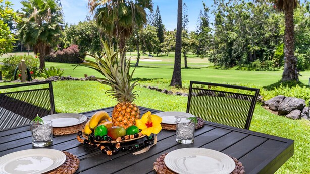 A table set outdoors with a tropical fruit arrangement, two chairs, and a golf course in the background.