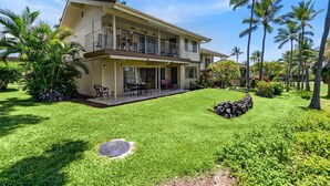 A two-story house with a balcony, surrounded by a well-maintained lawn and palm trees.
