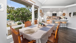 A dining area with a view of a pool and palm trees, a kitchen with white cabinets, and a dining table set with placemats and a vase.