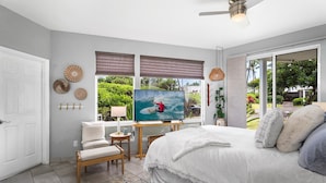 A bedroom with a large bed, a TV, a desk, and a view of greenery outside.