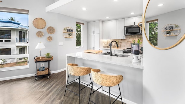 A modern kitchen with white cabinetry, a large island with bar stools, a TV mounted above the island, and decorative woven baskets on the wall.