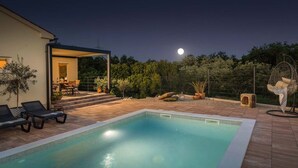Una piscina con lettini, una zona relax coperta all'aperto e un giardino recintato, di notte.
