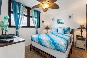 A bedroom with a bed, a ceiling fan, a nightstand, a lamp, and a decorative seahorse.
