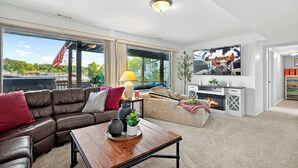 Un salon moderne avec un canapé en cuir, une table basse en bois et une cheminée. De grandes fenêtres offrent une vue sur l’extérieur.