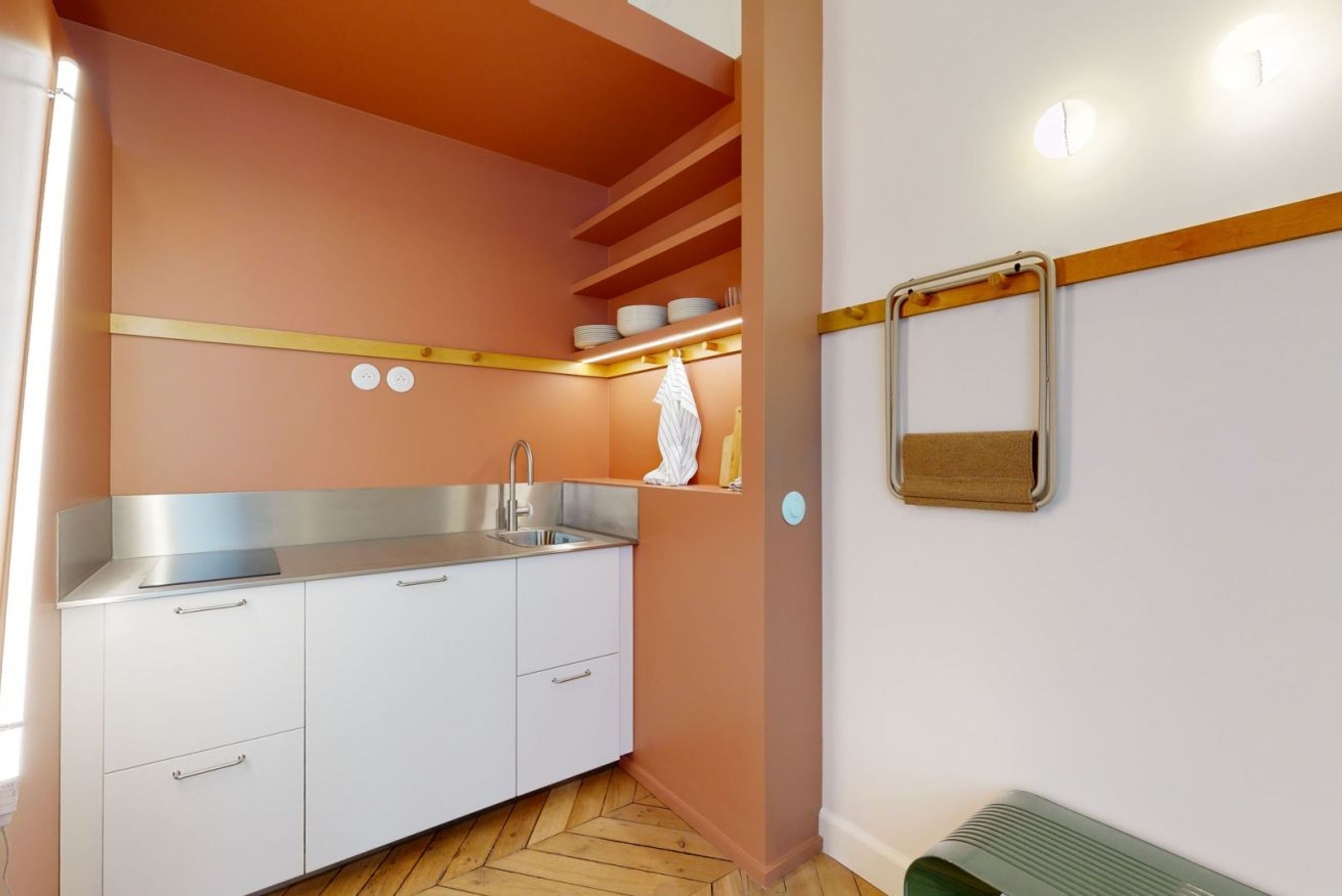 A compact kitchen with white cabinets, a stainless steel sink, and a wooden herringbone floor.
