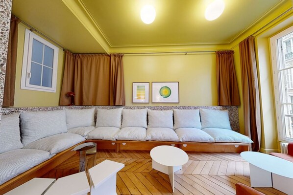 A room with a large L-shaped sofa, a small round table, and a window with curtains.