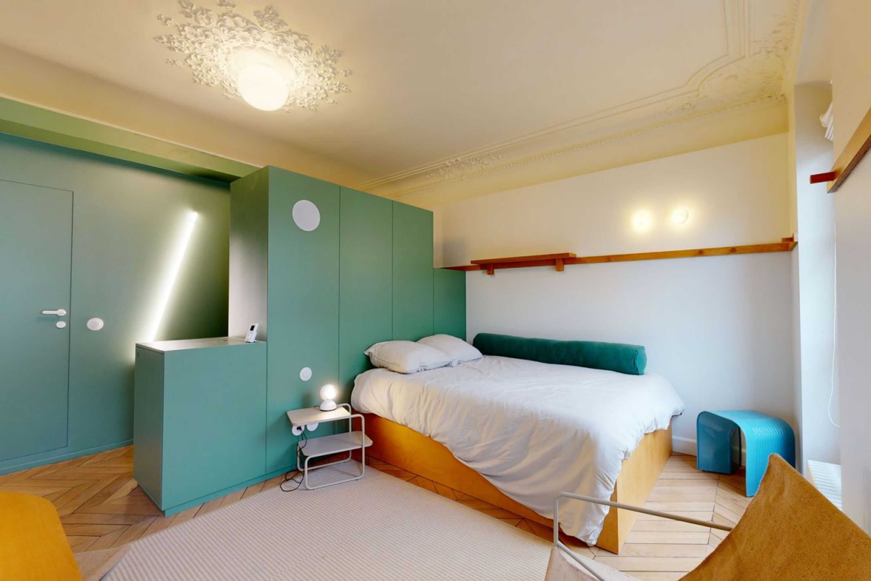Un dormitorio con cama, mesita de noche, armario y un taburete pequeño.