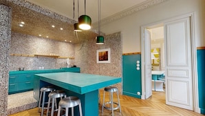 A modern kitchen with a teal island, bar stools, granite backsplash, and pendant lighting. - Delightful 1-bed Studio w Shared Co-working Space (Paris)