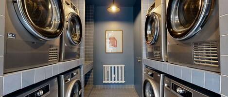 A laundry room with multiple front-loading washing machines and dryers, a tiled floor, and a ceiling light.