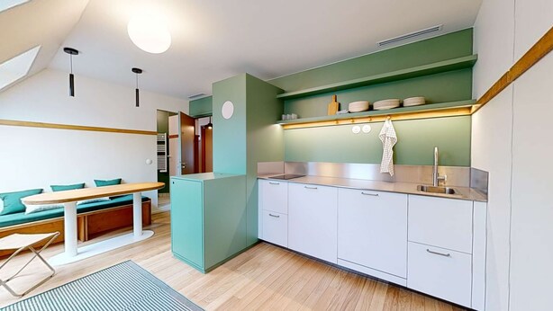 Een compacte keuken met een eethoek, voorzien van een inbouwfornuis, witte kasten en een klein keukeneiland.