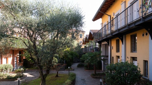 A courtyard with a cobblestone path, surrounded by buildings with balconies and a tree. - Beautiful Two-Level One-Bedroom Apartment – Mirable PM (Milan)