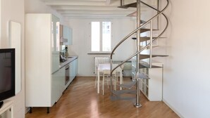 A modern kitchen with white cabinets and a built-in oven, a dining area with a white table and chairs, and a spiral staircase leading to an upper floor. - Beautiful Two-Level One-Bedroom Apartment – Mirable PM (Milan)