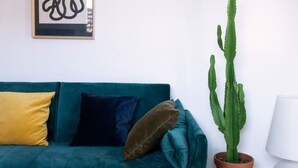 A teal sofa with yellow and brown cushions, a potted cactus, and a framed abstract artwork on the wall. - Beautiful Two-Level One-Bedroom Apartment – Mirable PM (Milan)