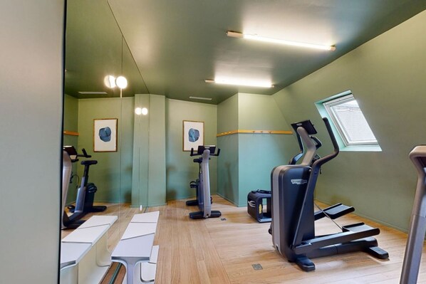 Un gimnasio con máquinas de cardio, espejos y un ventanal.