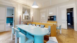A modern dining area with a light blue table and white chairs, a wooden bench with cushions, and pendant lighting. - Charming 2-bed Flat w Shared Spaces (Paris)