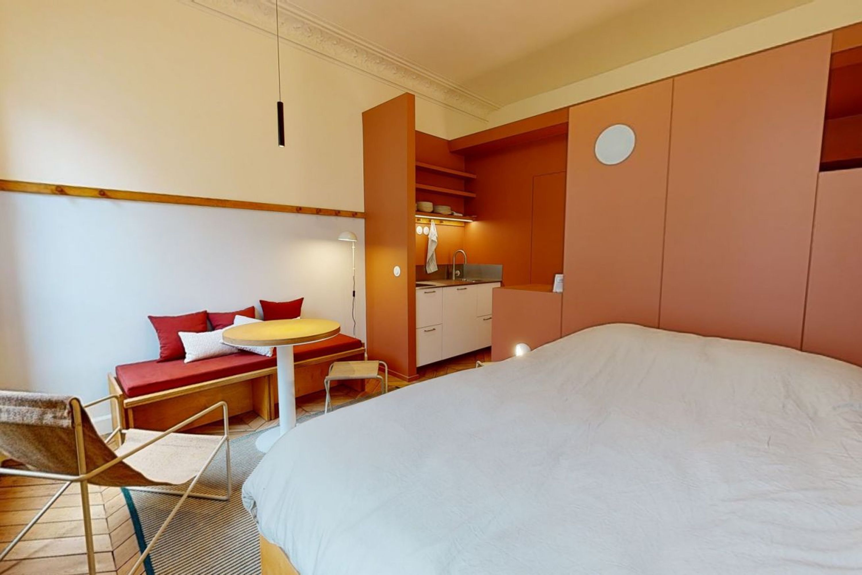 A compact hotel room with a large bed, a small seating area with a table, and a kitchenette.