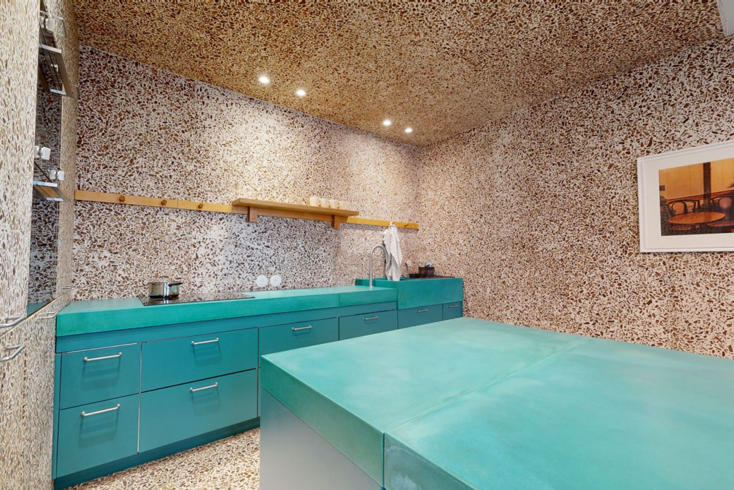 Een keuken met een gevlekt spatwandje, blauwgroene keukenkastjes, en een houten plank boven de gootsteen.