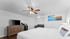 A bedroom with a large bed, a ceiling fan, a TV, a dresser, and a painting on the wall.