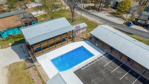 An aerial view of a building with a swimming pool, a covered outdoor area, and a parking lot.