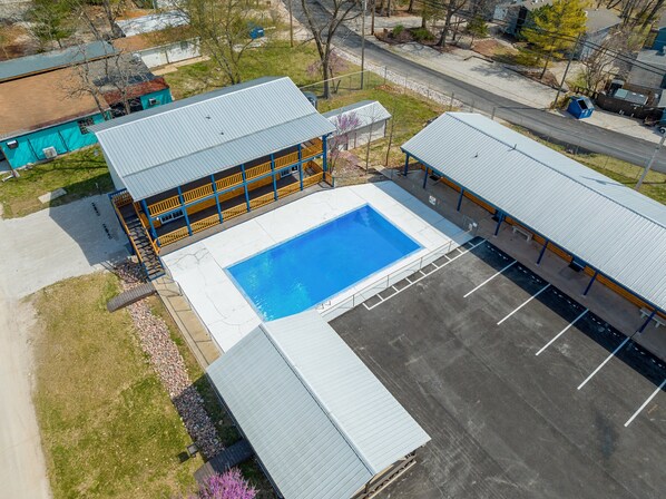 Vue aérienne d’un bâtiment doté d’une piscine, d’un espace extérieur couvert et d’un parking.
