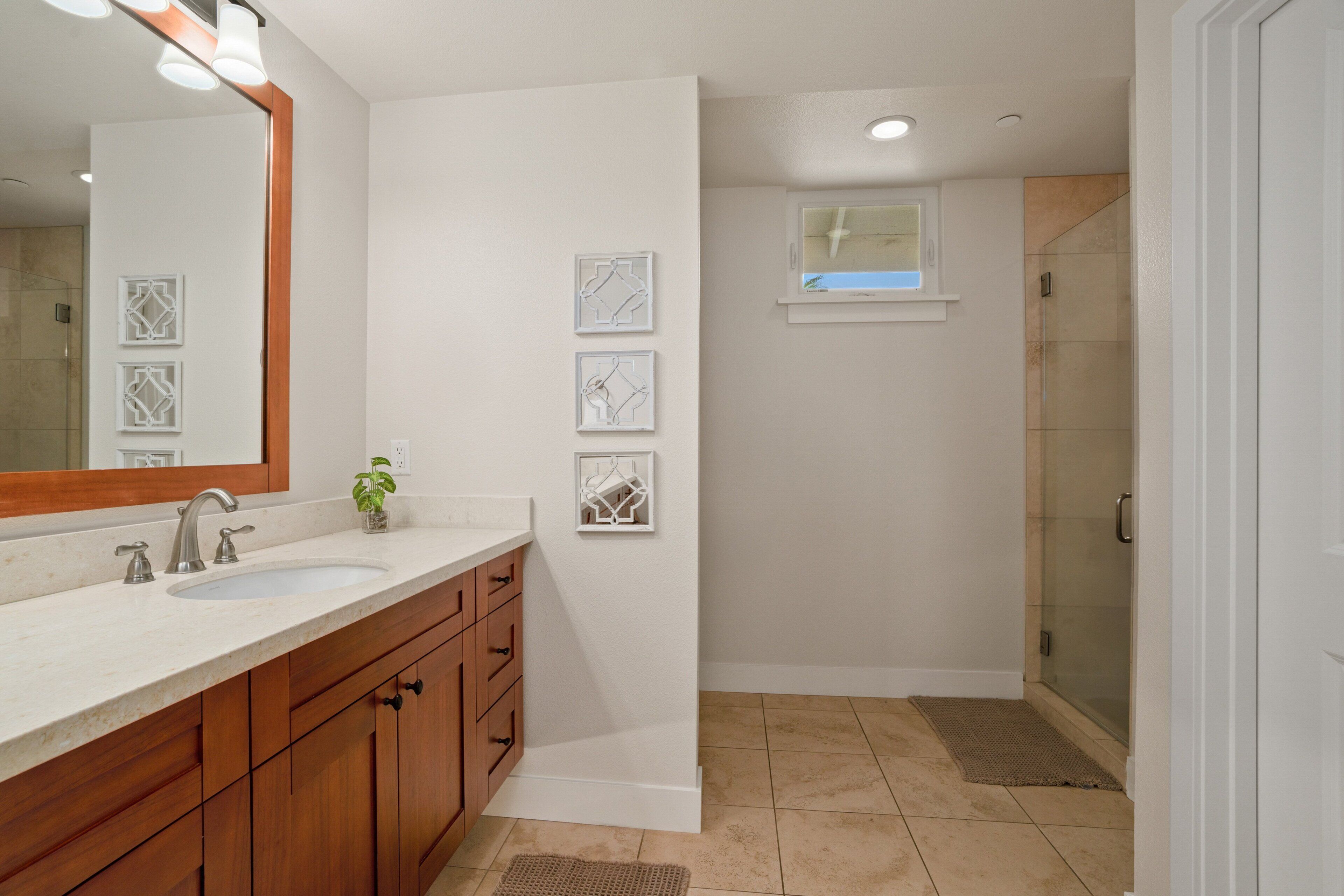 A bathroom with a large mirror, two sinks, wooden cabinets, and a shower area.