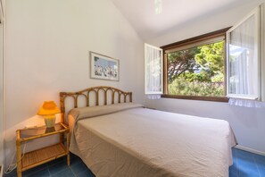 Une chambre à coucher avec un lit, une table de chevet avec une lampe, une fenêtre avec des rideaux et un tableau accroché au mur.