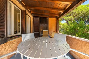 Un espace extérieur abrité, aménagé avec une table ronde et des chaises, un plafond en bois et une vue sur la verdure.