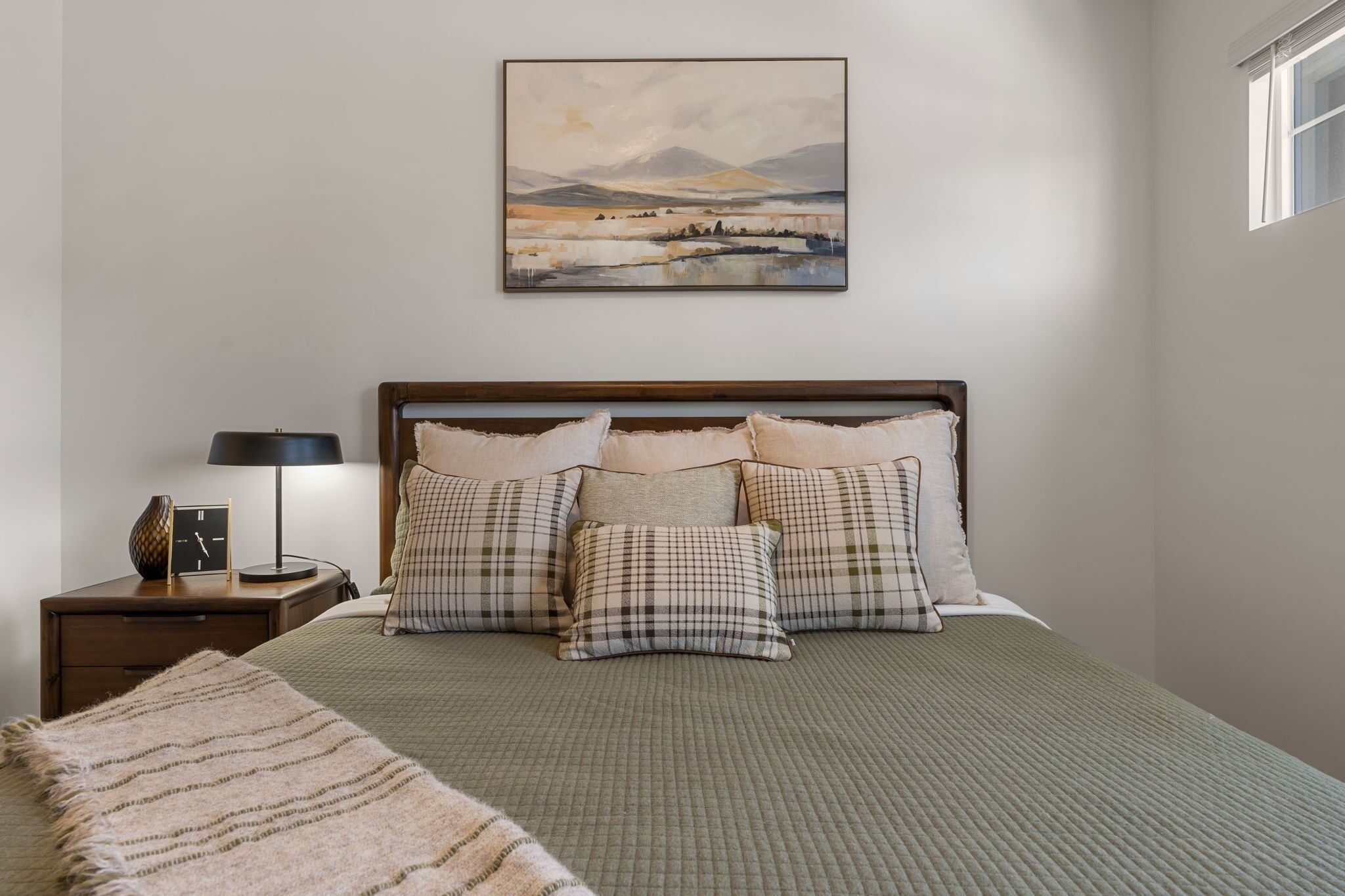Une chambre à coucher bien rangée, avec un lit, des oreillers, une table de chevet avec une lampe et un tableau accroché au mur.